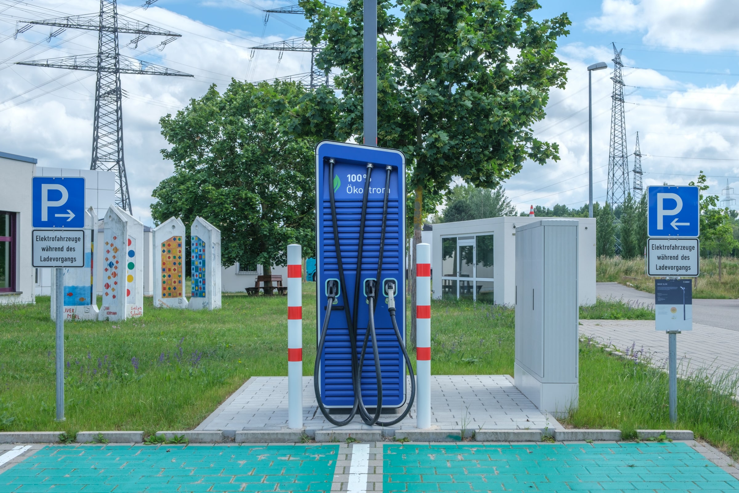 A blue electric-vehicle charger stands between marked bays beneath power lines.