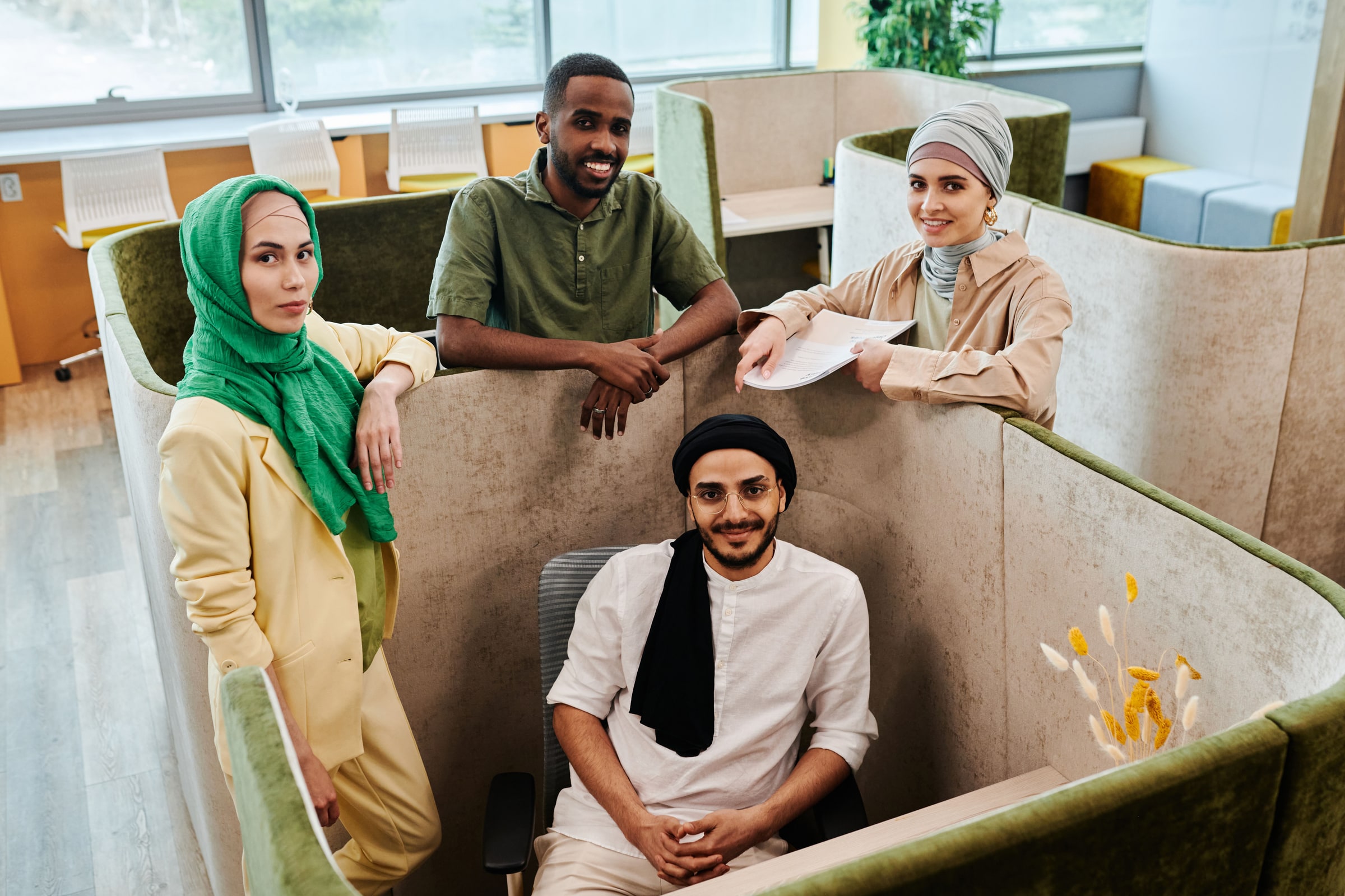 Four colleagues pose together inside a modern office, including two women wearing headscarves and two men.