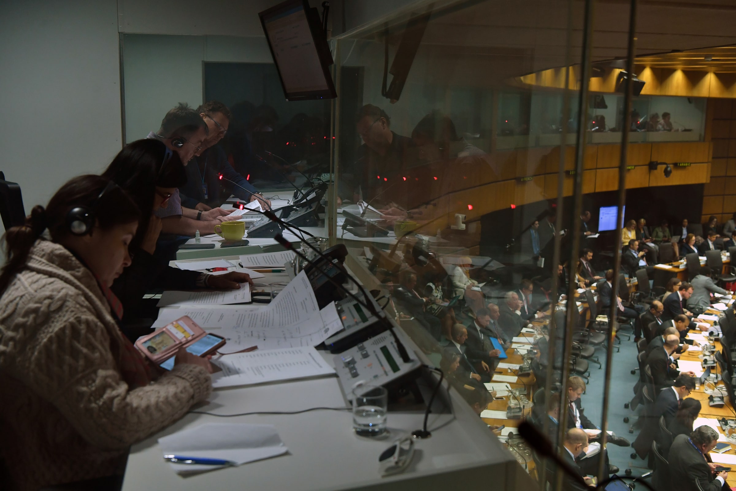 Interpreters wearing headsets work with documents inside a booth overlooking an IAEA meeting in Vienna.
