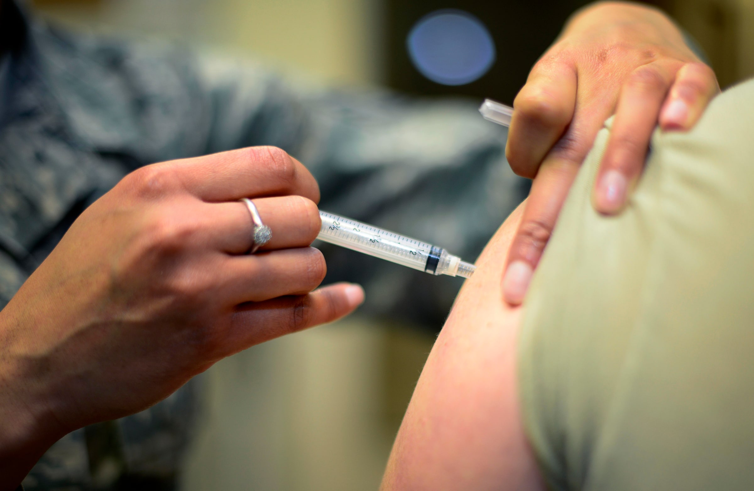 A clinician administers a vaccination into an adult’s upper arm.