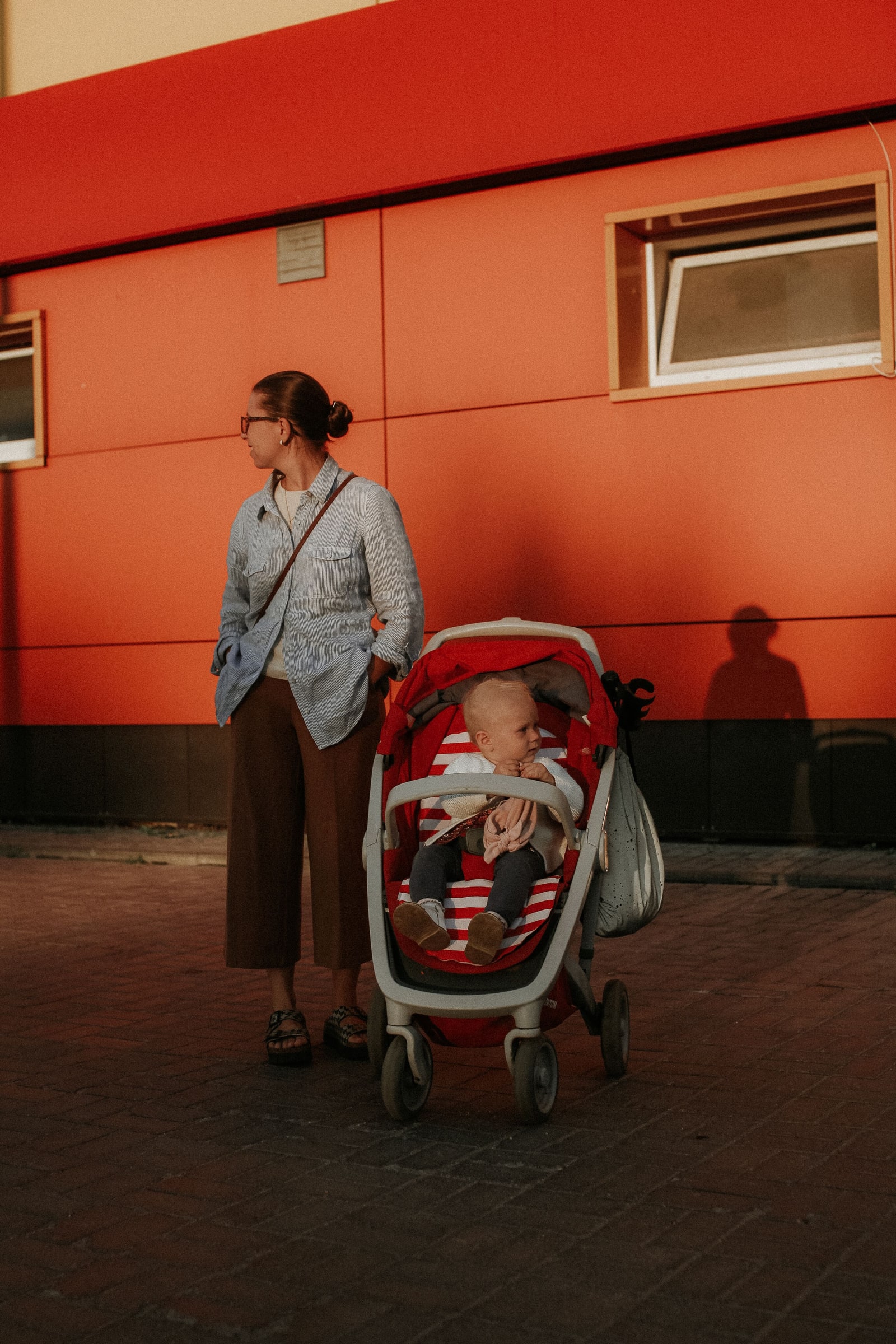 A woman stands beside a baby seated in a stroller outdoors.