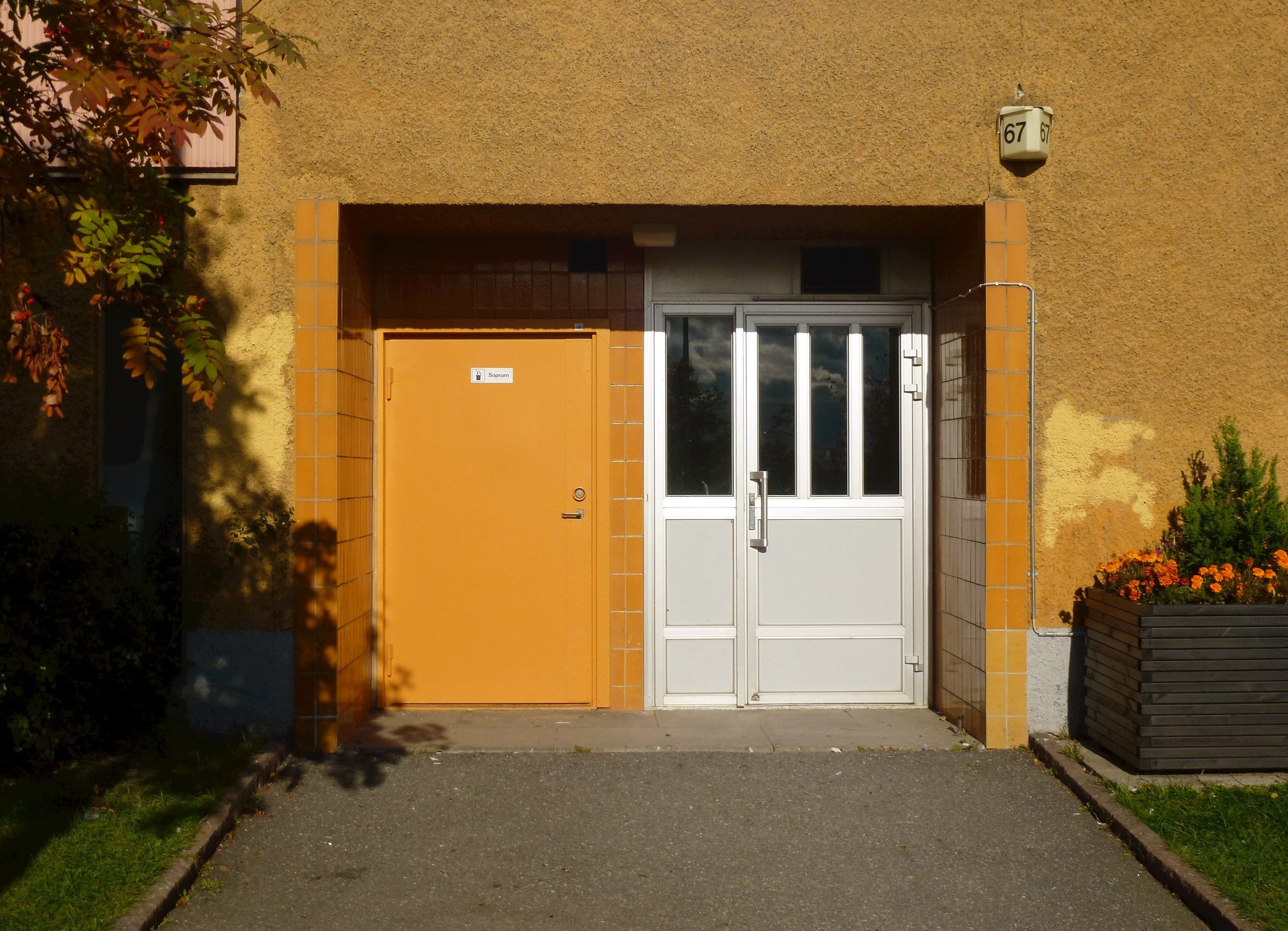 An apartment-building entrance with a white glazed door in a yellow wall at Henriksdalsberget in Nacka.