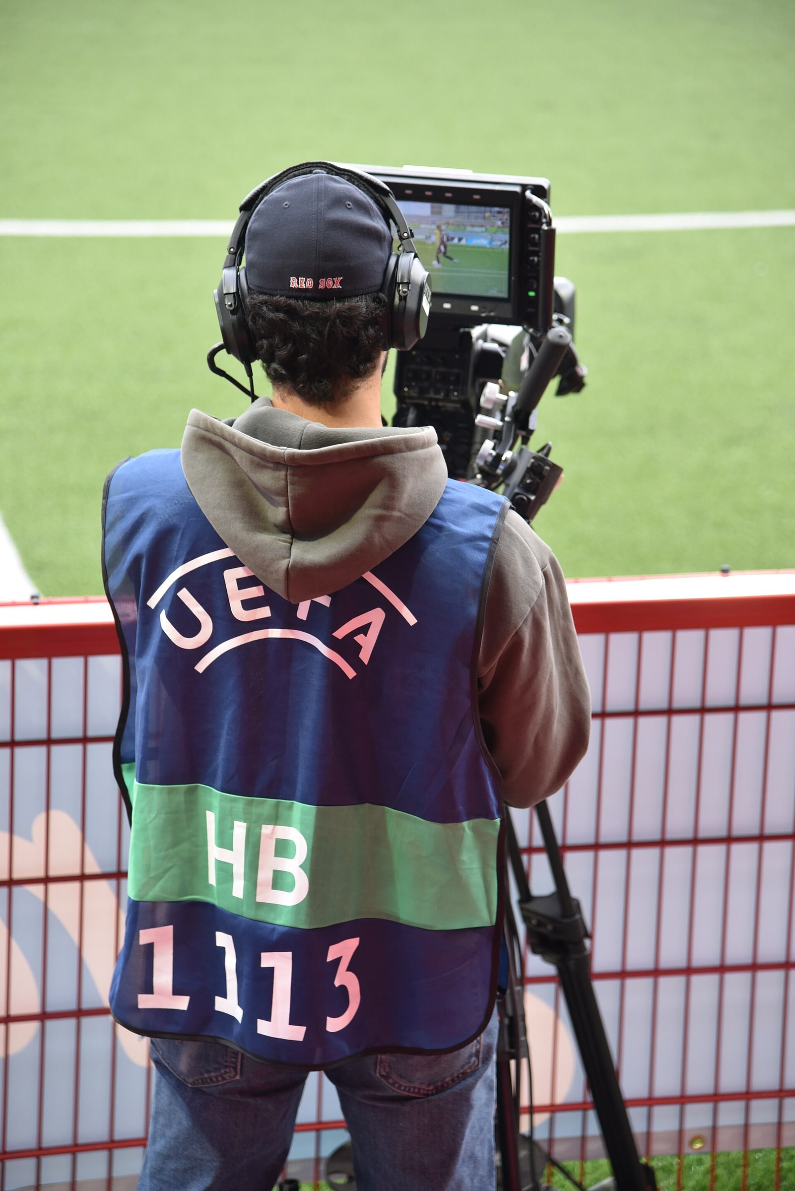 A television camera operator films a football match from behind a barrier.