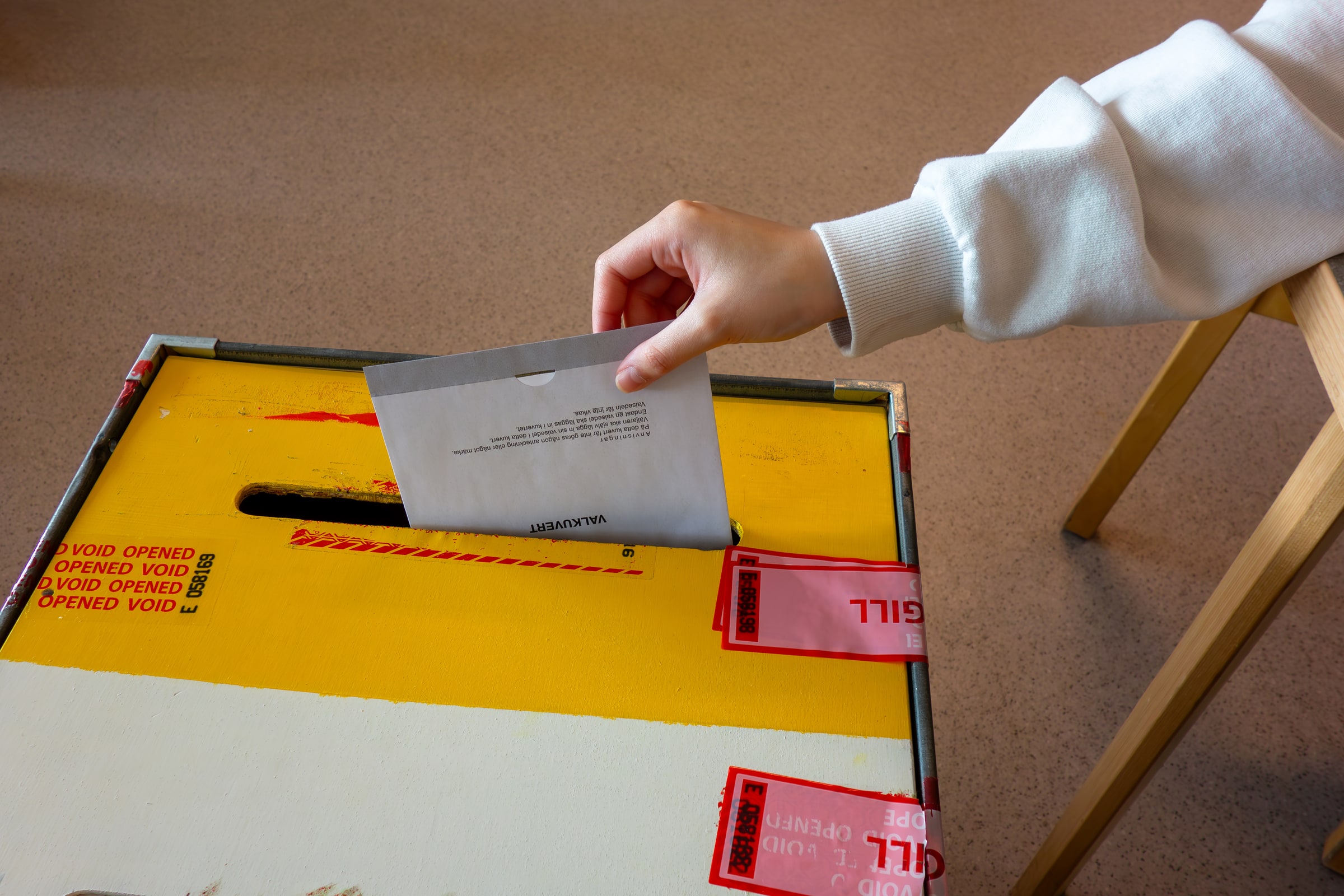 A hand places a sealed ballot envelope into a Swedish ballot box.