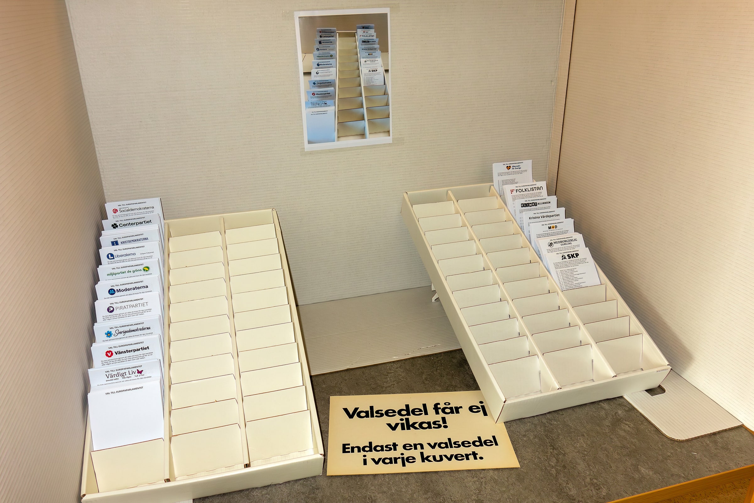 Multiple Swedish party ballots sit in racks inside an empty ballot-selection stand.