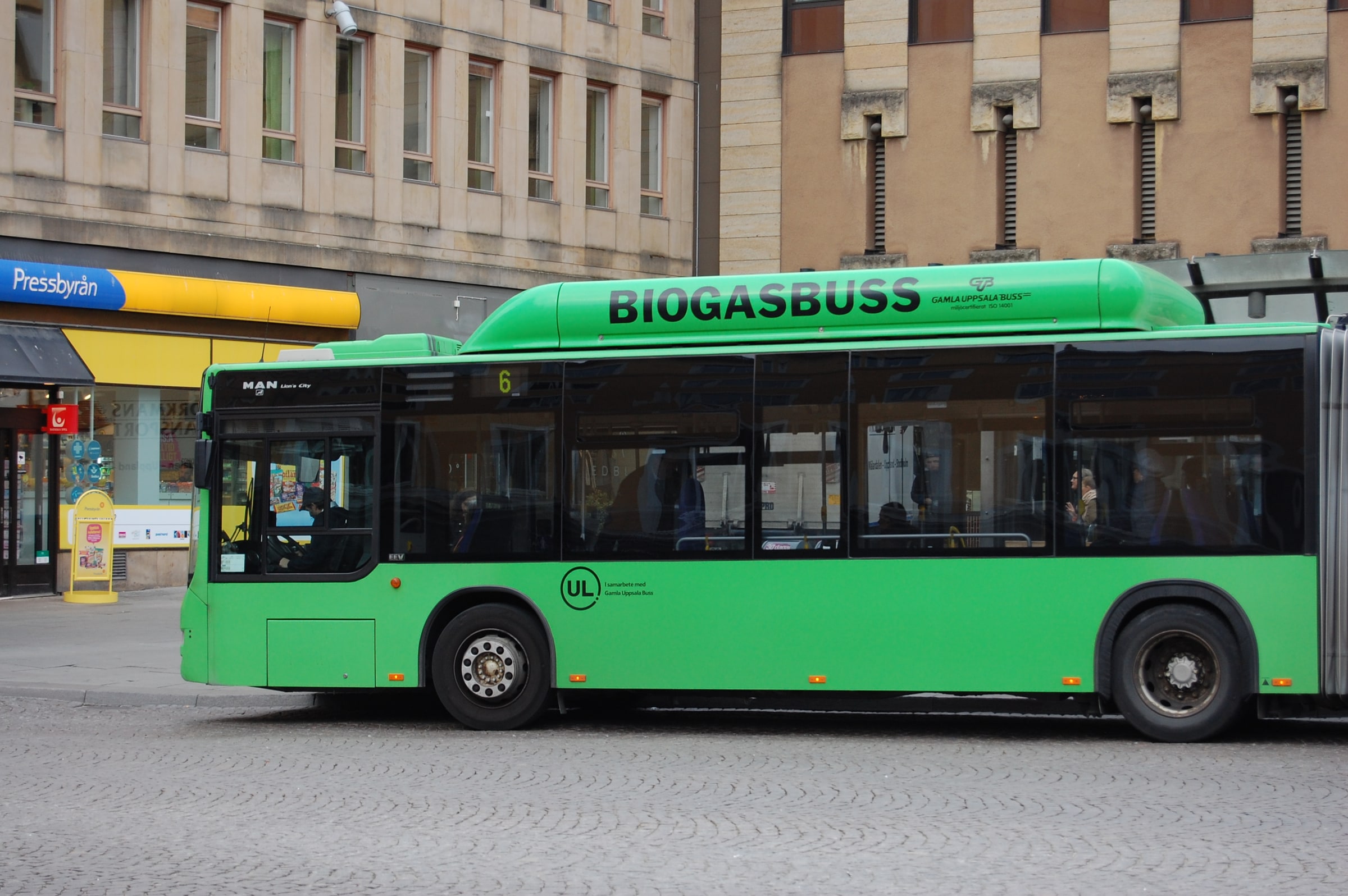 A green Uppsala city bus carries passengers past Stora torget.