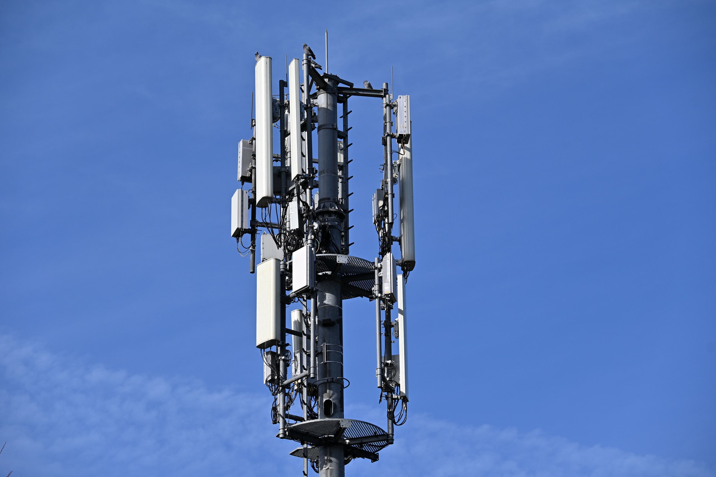 A mobile communications mast with multiple panel antennas against a blue sky.